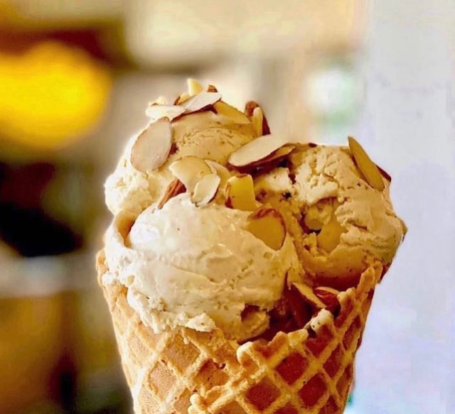 A waffle cone piled with a pale scoop and toasted almonds.