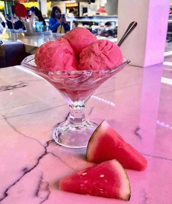 Bright pink Italian ice in a glass coupe with fresh fruit beside it.